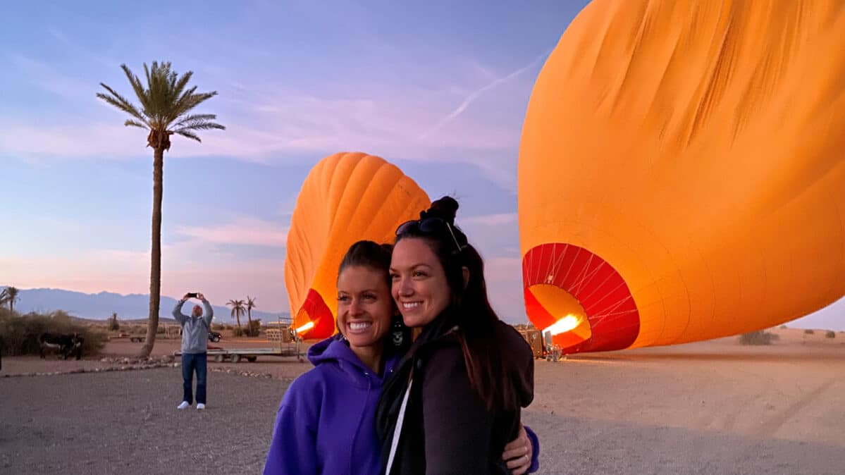 Two woman posing in front of a hot air balloon.