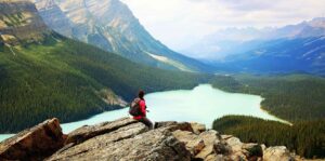 A young person sitting on a cliff looking out at a body of water.