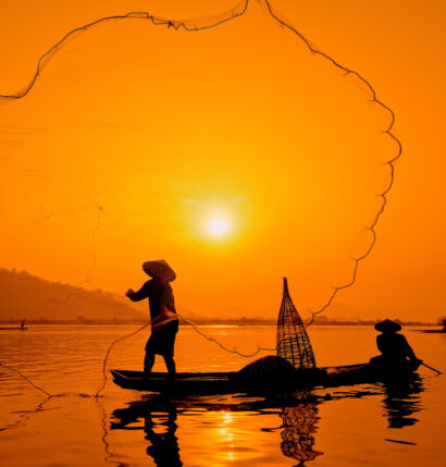 A silhouette of two people on a boat with a fishing net.
