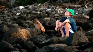 Boy sitting next to a seal in the Galapagos.
