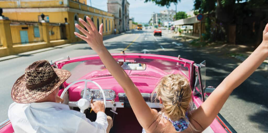 Travelers driving through the colorful streets of Havana Cuba in a classic car