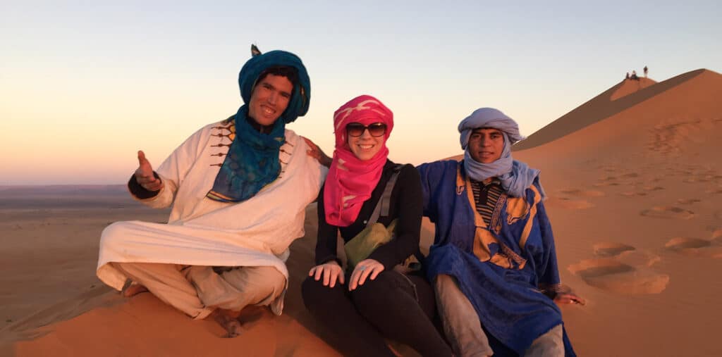 Woman resting on a sand dune in Morocco with her local guides