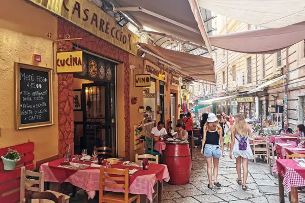 Photo depicts customers outside Palermo cafe with cobblestone streets and red checkered tablecloths