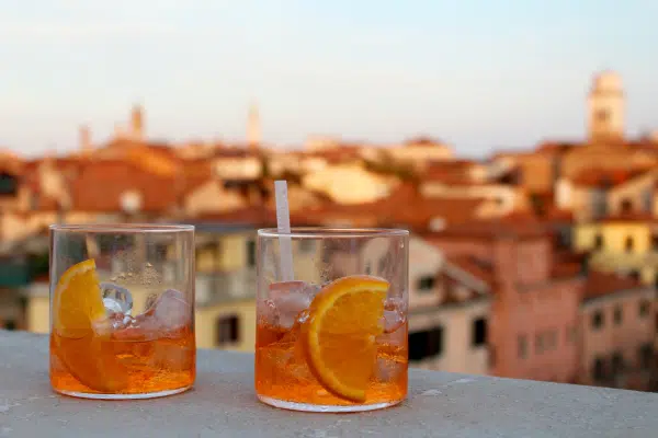 Two orange-colored cocktails on a ledge looking over a city. 