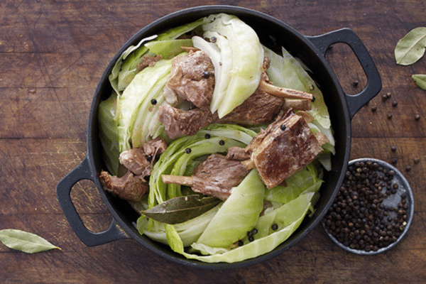 Fårikål being cooked in a dutch over, with a plate of peppercorns next to it