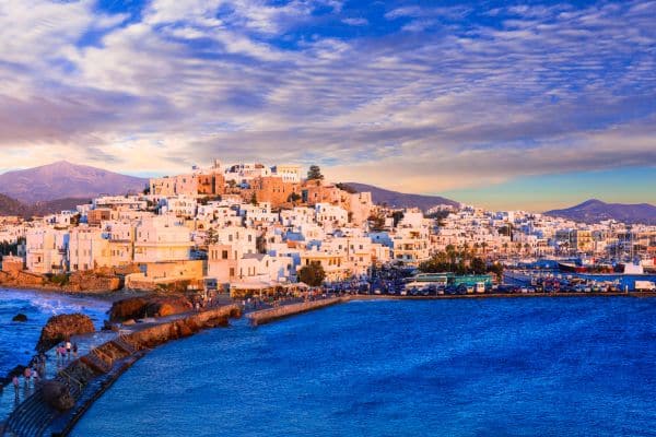 Travelers walking along the coast of Naxos with whitewashed houses in the background of Greece