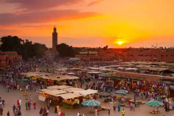 A lively market in Marrakesh shows visitors and vendors mingling as the sun sets