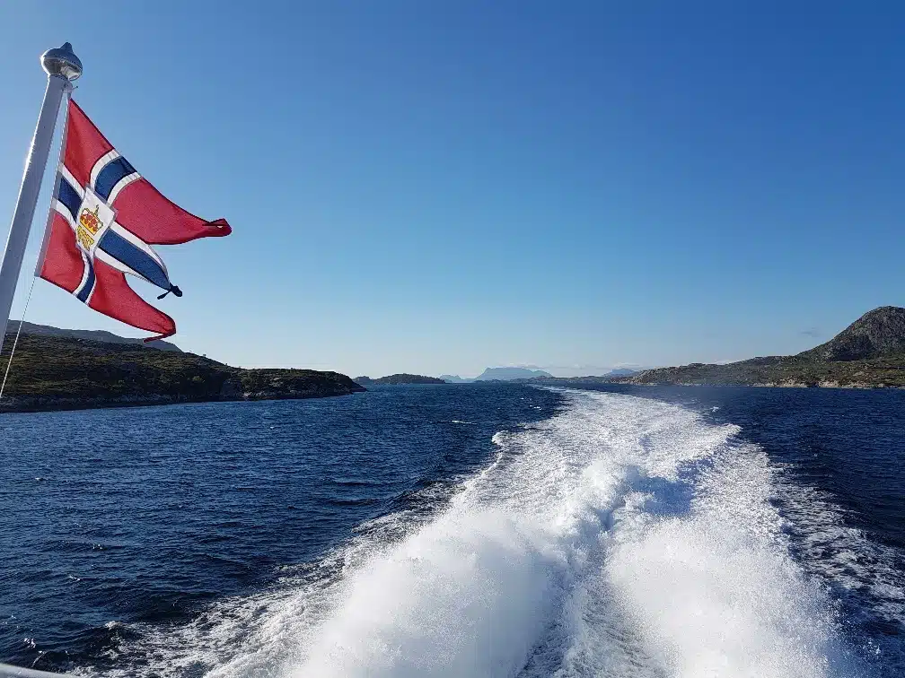 The Norwegian flag flying from the back of a boat on the water