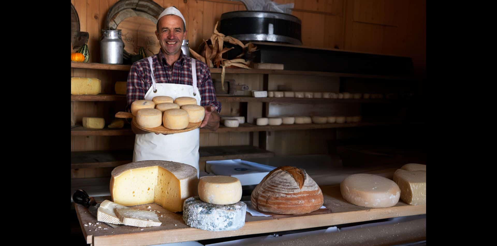Cheesemonger showing off his Italian cheeses in his rustic shop, Dolomites, Italy.