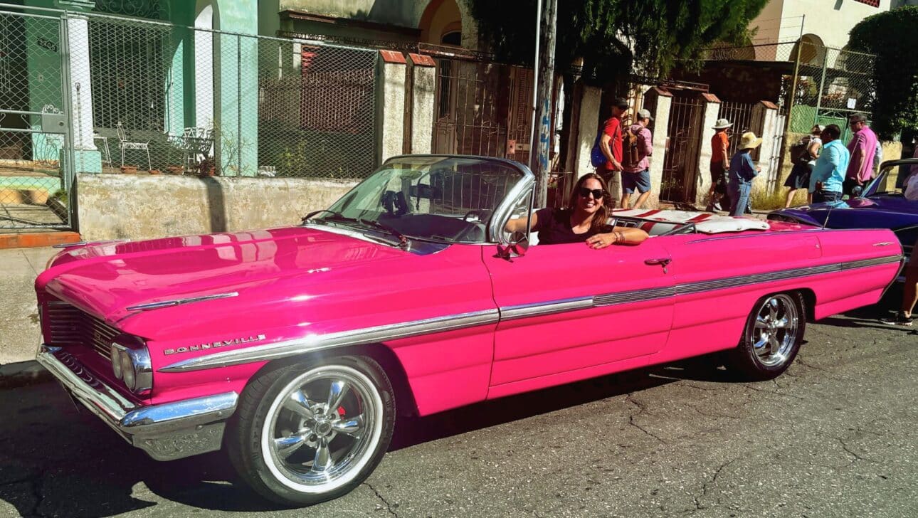 Traveler enjoying a ride in a pink classic car in Havana, Cuba. She's enjoying a Walking tour of Cuba.