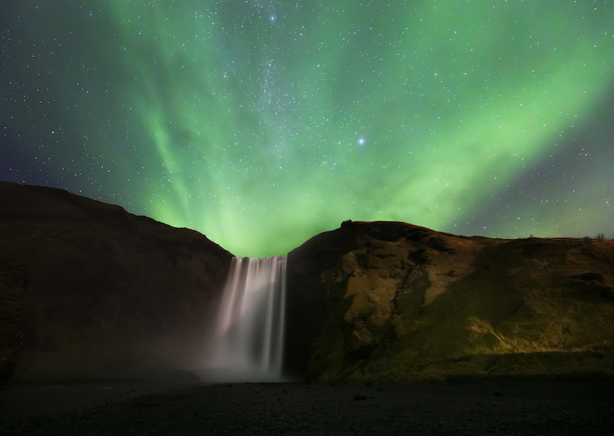Iceland waterfall at night with the northern lights and stars green glow