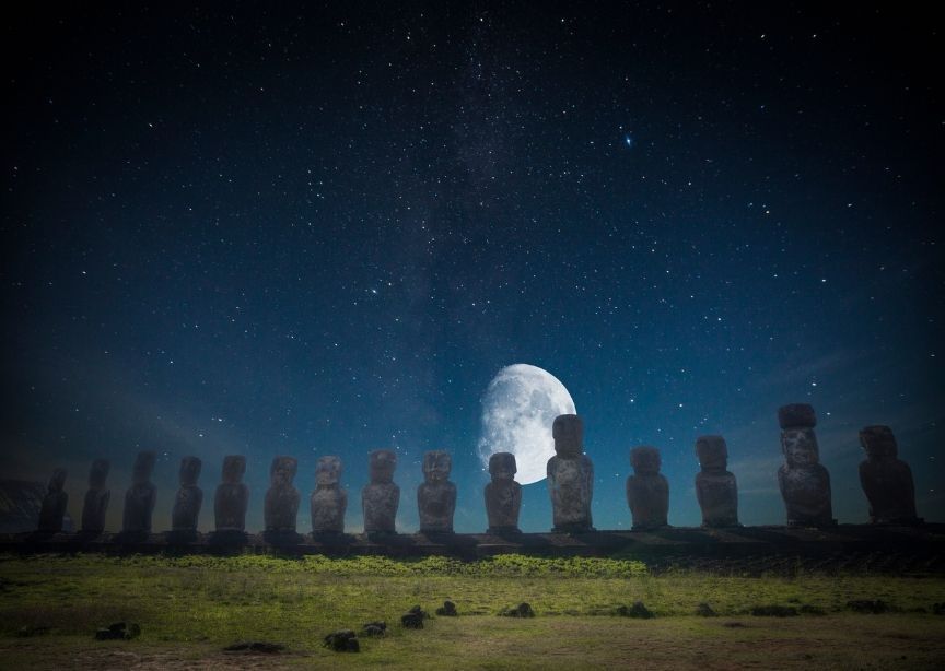 Easter Island Chile Moai Statues at night with moon and stars, grass in forefront